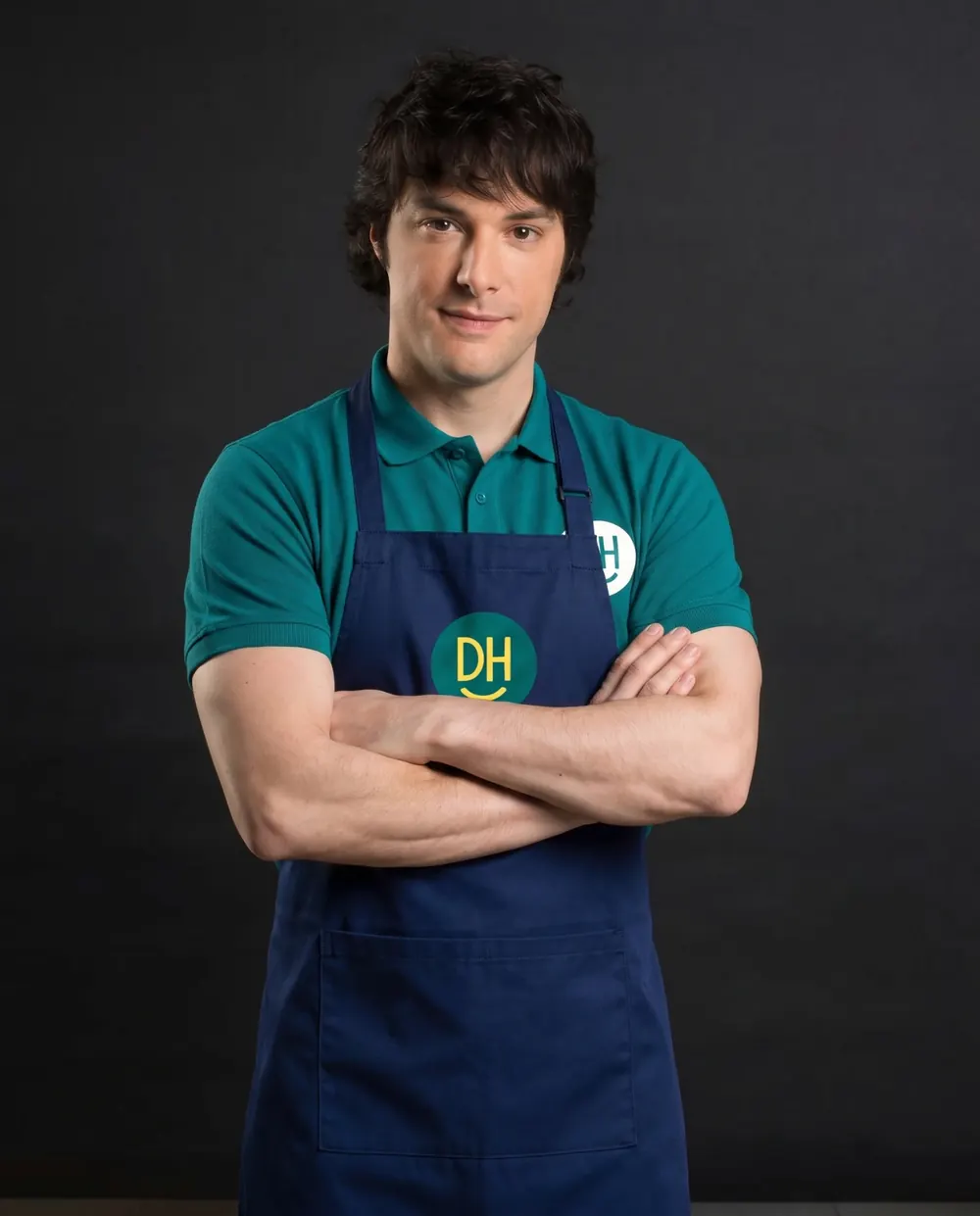 A Daily Heroes team member in a navy apron, arms folded, smiling