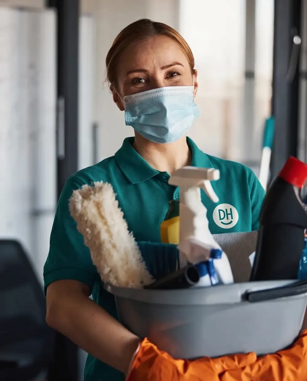A Daily Heroes cleaner in a mask carrying cleaning supplies