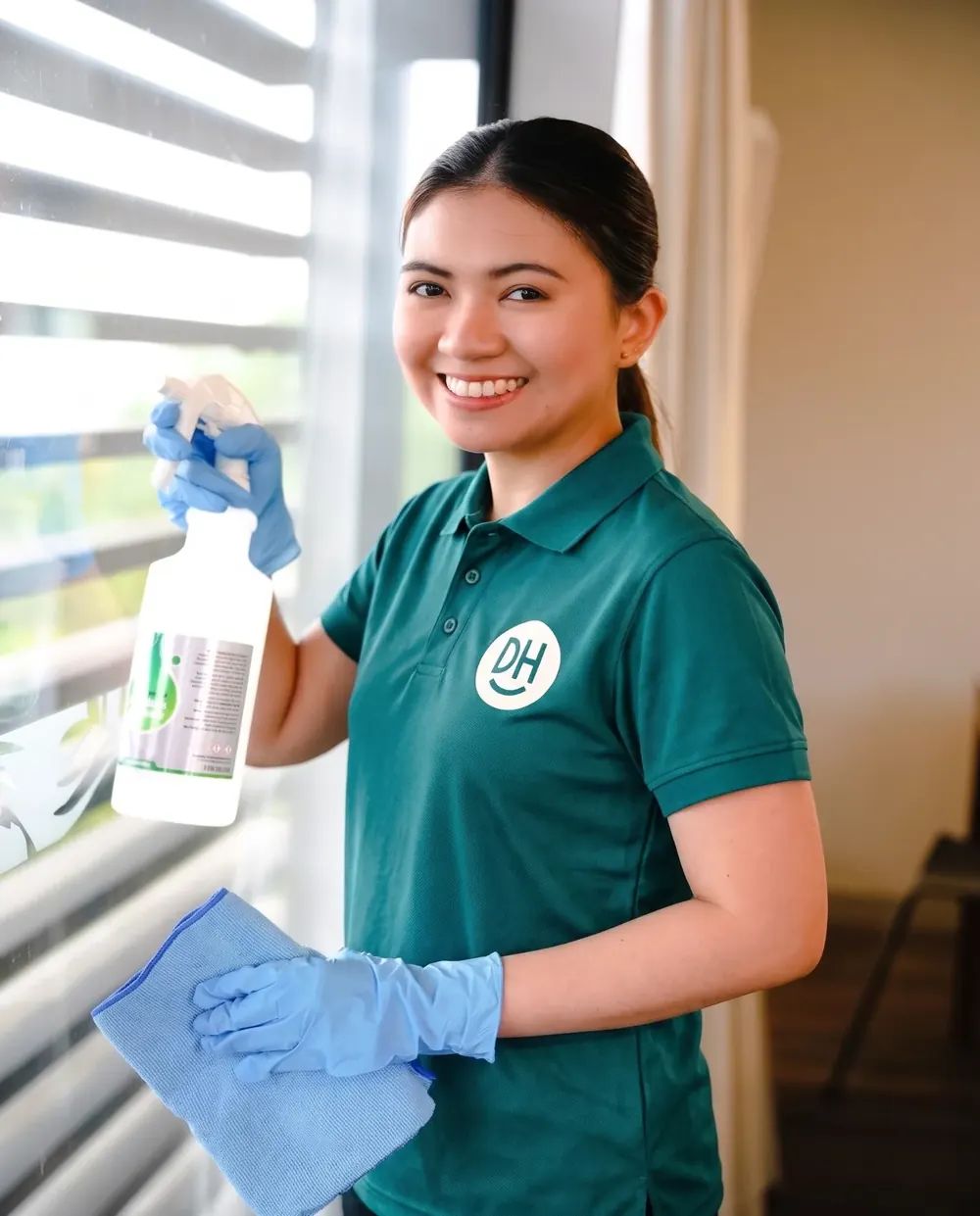 A smiling Daily Heroes cleaner with a spray bottle and cloth