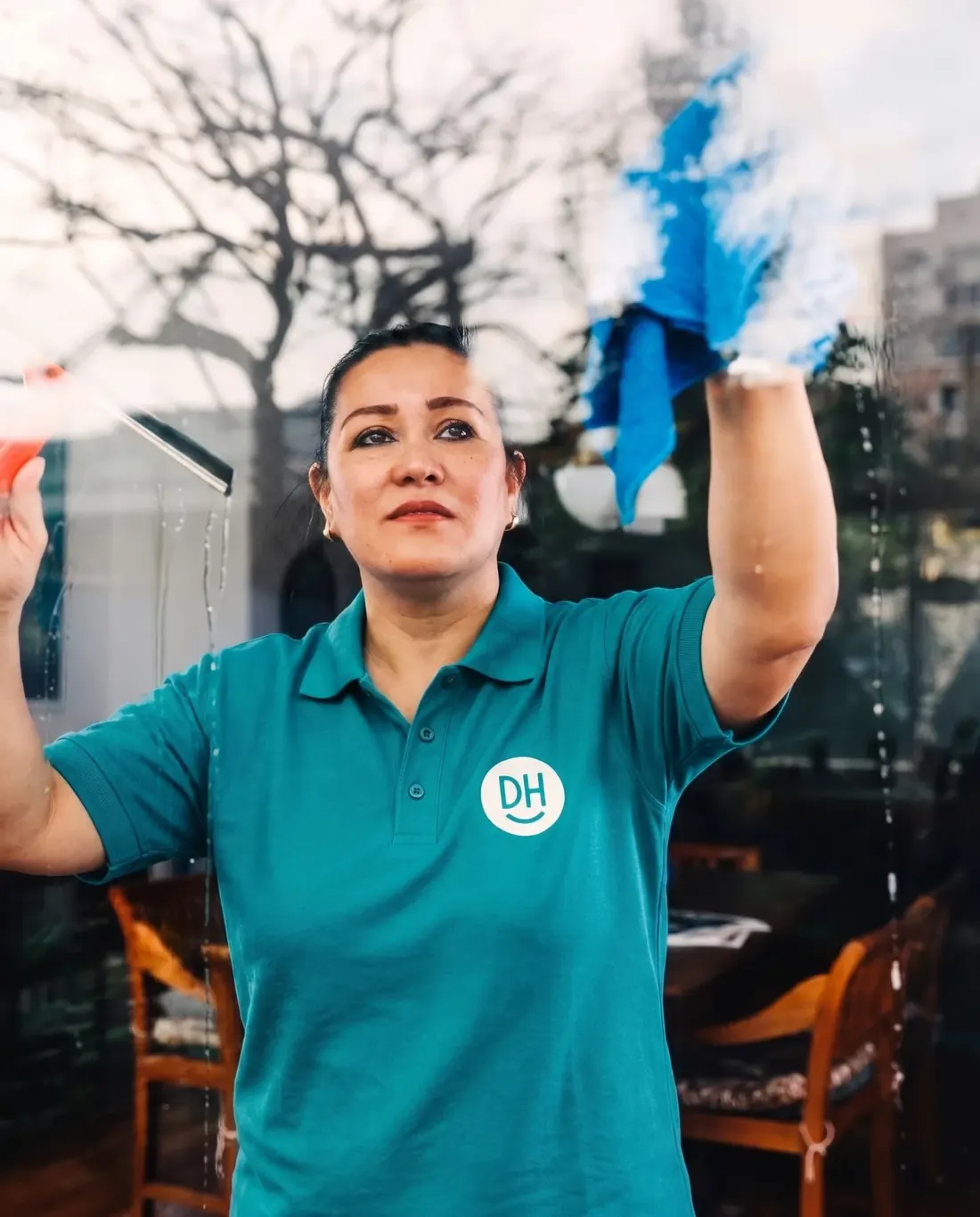 A Daily Heroes worker cleaning a large window with a squeegee and cloth